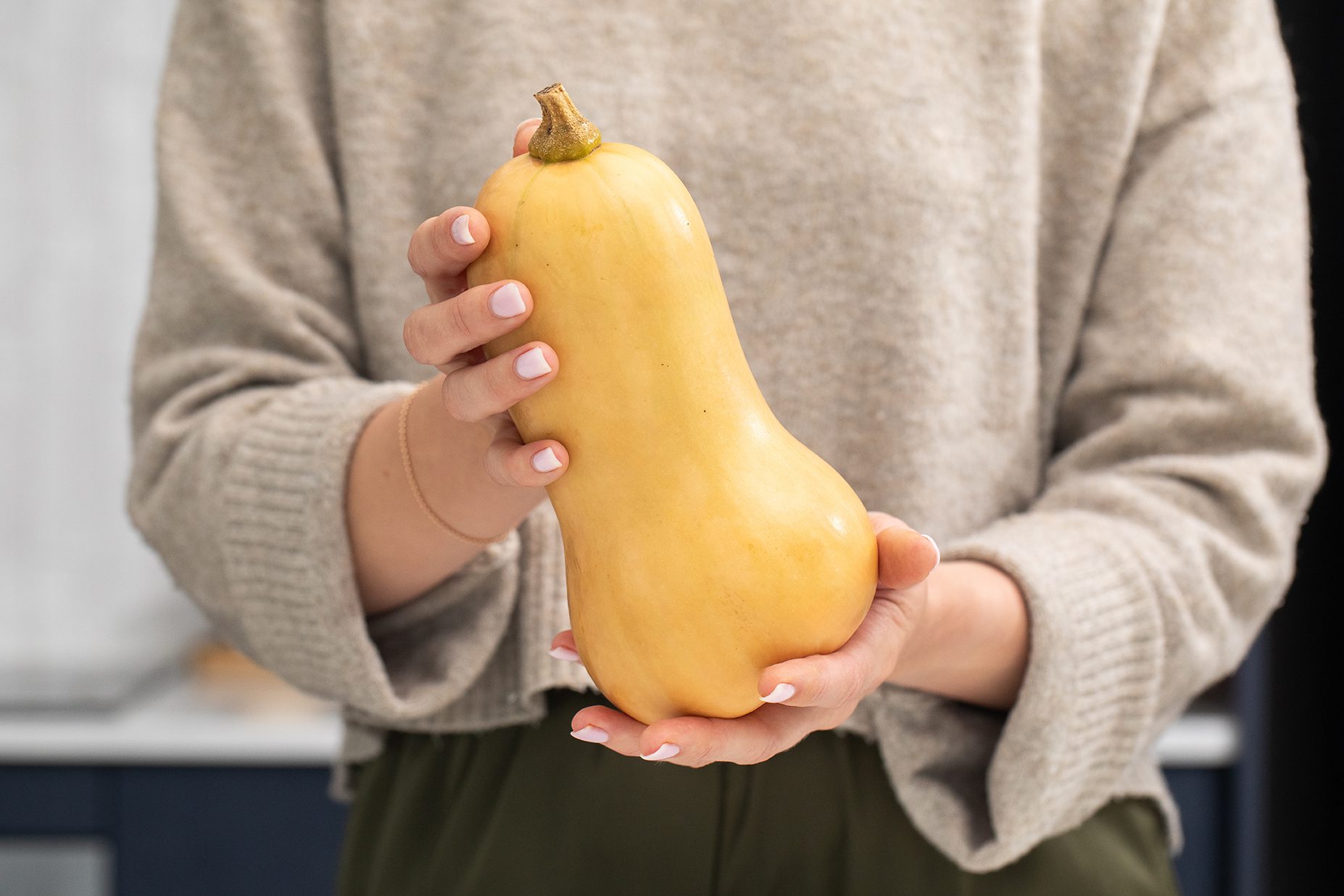 Person holding butternut squash in kitchen setting.