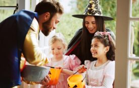 Two children trick or treating with a female parent. A man at the door hands out treats.