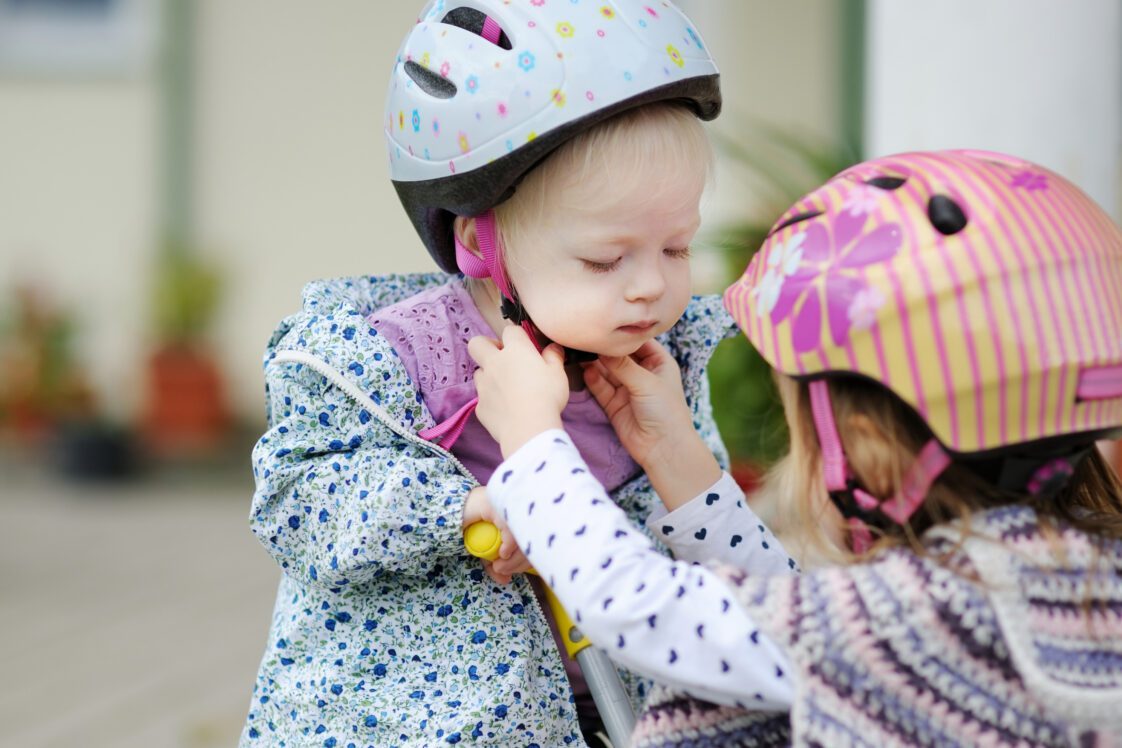 Little girl helping her sister put on a bicycle helmet.