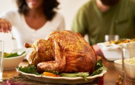 A closeup of a Thanksgiving turkey on a dinner table with a man and woman seen in the background.