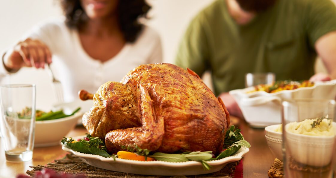 A closeup of a Thanksgiving turkey on a dinner table with a man and woman seen in the background.