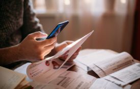 A man pays utility bills online using a QR code in an app using a smartphone in the kitchen. Close-up of hands, phone, and bills.