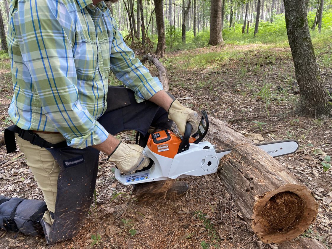 A man demonstrating proper chainsaw safety while cutting a log.
