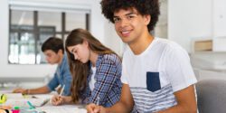 A group of teenagers sitting at a table in school which one male student looking into the camera.