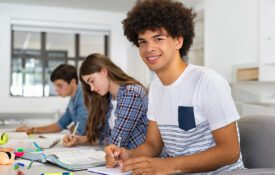 A group of teenagers sitting at a table in school which one male student looking into the camera.