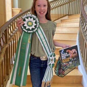 Alaina Knight with her ribbon, sash, book, and egg gather basket. All were prizes she received for winning first place in the Golden Egg Contest.