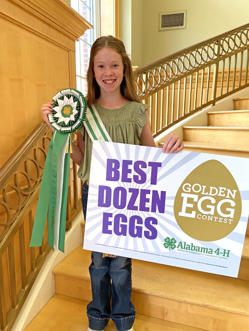 Alaina Knight with her first-place ribbon and a sign that reads Best Dozen Eggs. She received both for earning first place in the Golden Egg Contest.