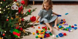 A little girl playing with colorful building blocks next to the Christmas tree.