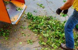 A closeup of the back of a wood chipper with a ground worker partially in the photo.