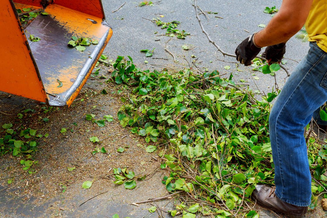 A closeup of the back of a wood chipper with a ground worker partially in the photo.