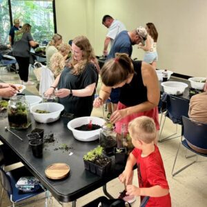 A large group of Third Thursday attendees of all ages work on individual terrariums.