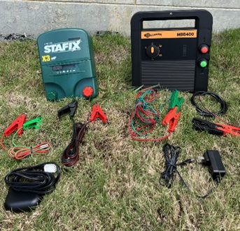 Electric fence charging boxes lying on the ground with the wires in front of them.