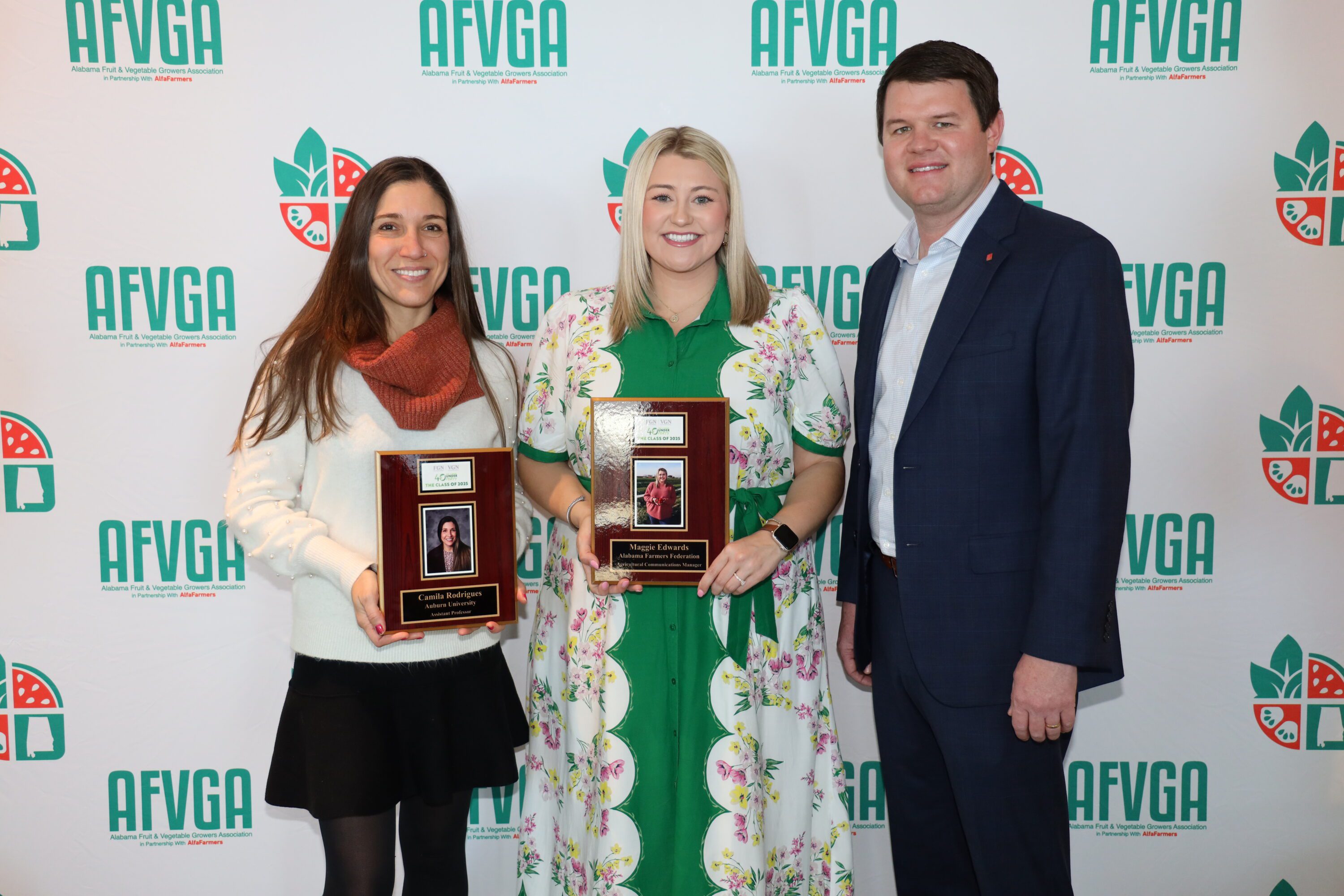Camila Rodrigues and Maggie Edwards holding awards and standing with Blake Thaxton.