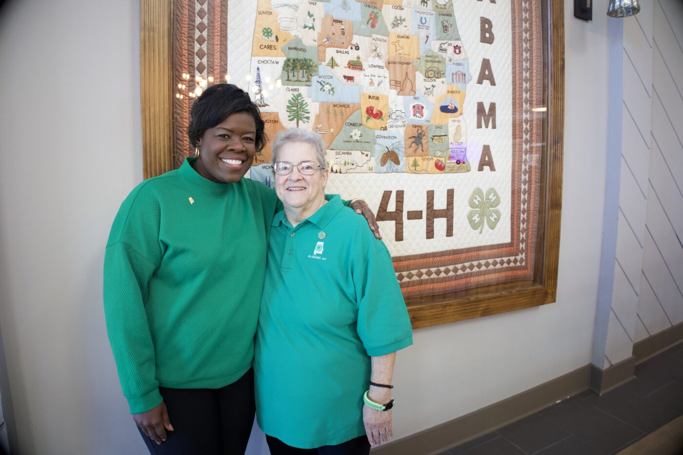 Joy Scott and Betty Gottler standing in front of an Alabama quilt that hangs at the Alabama 4-H Center.