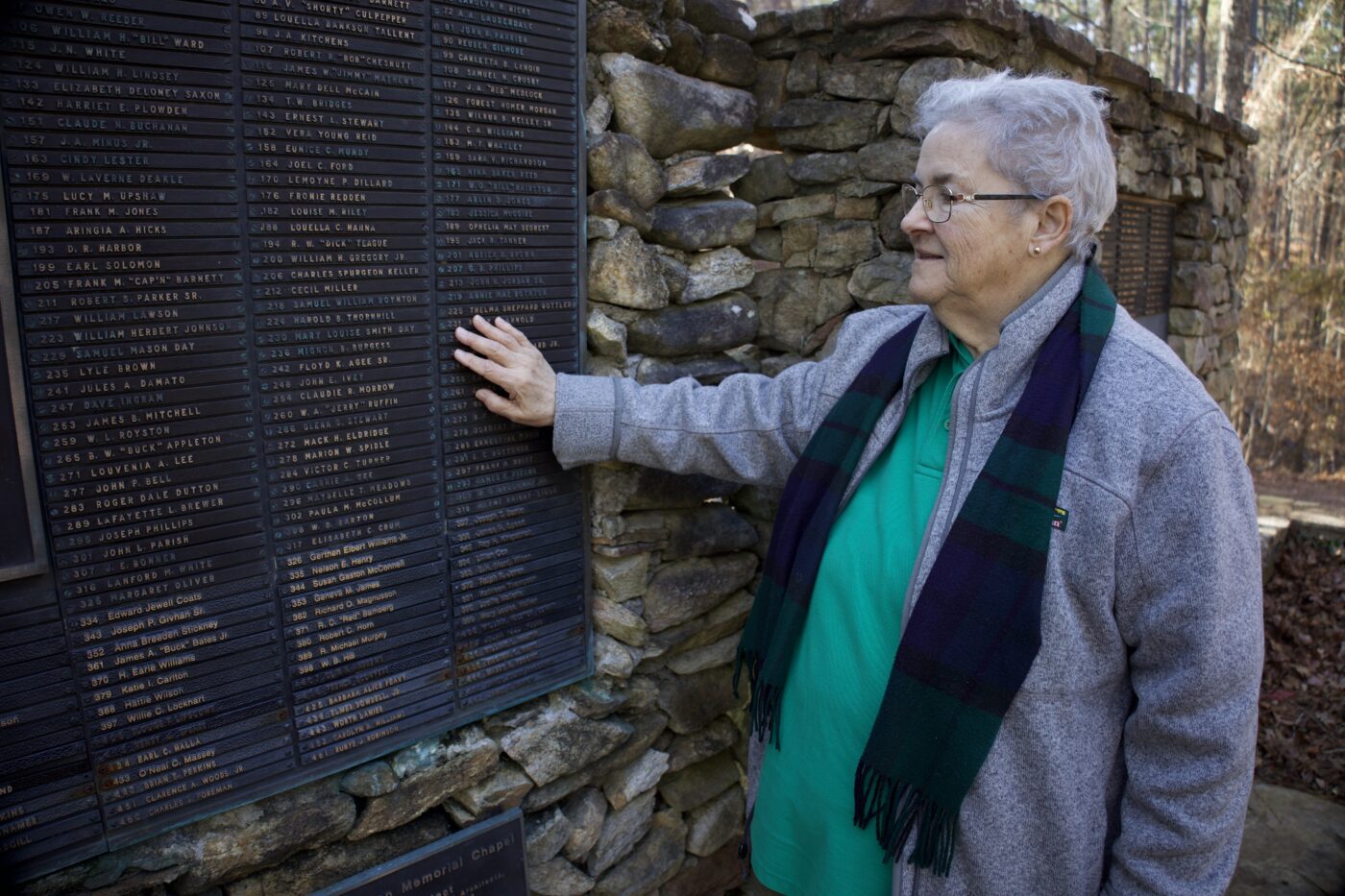 Betty Gottler standing at the Alabama 4-H Center chapel. Her hand is placed on her mother's name on a memorial wall.