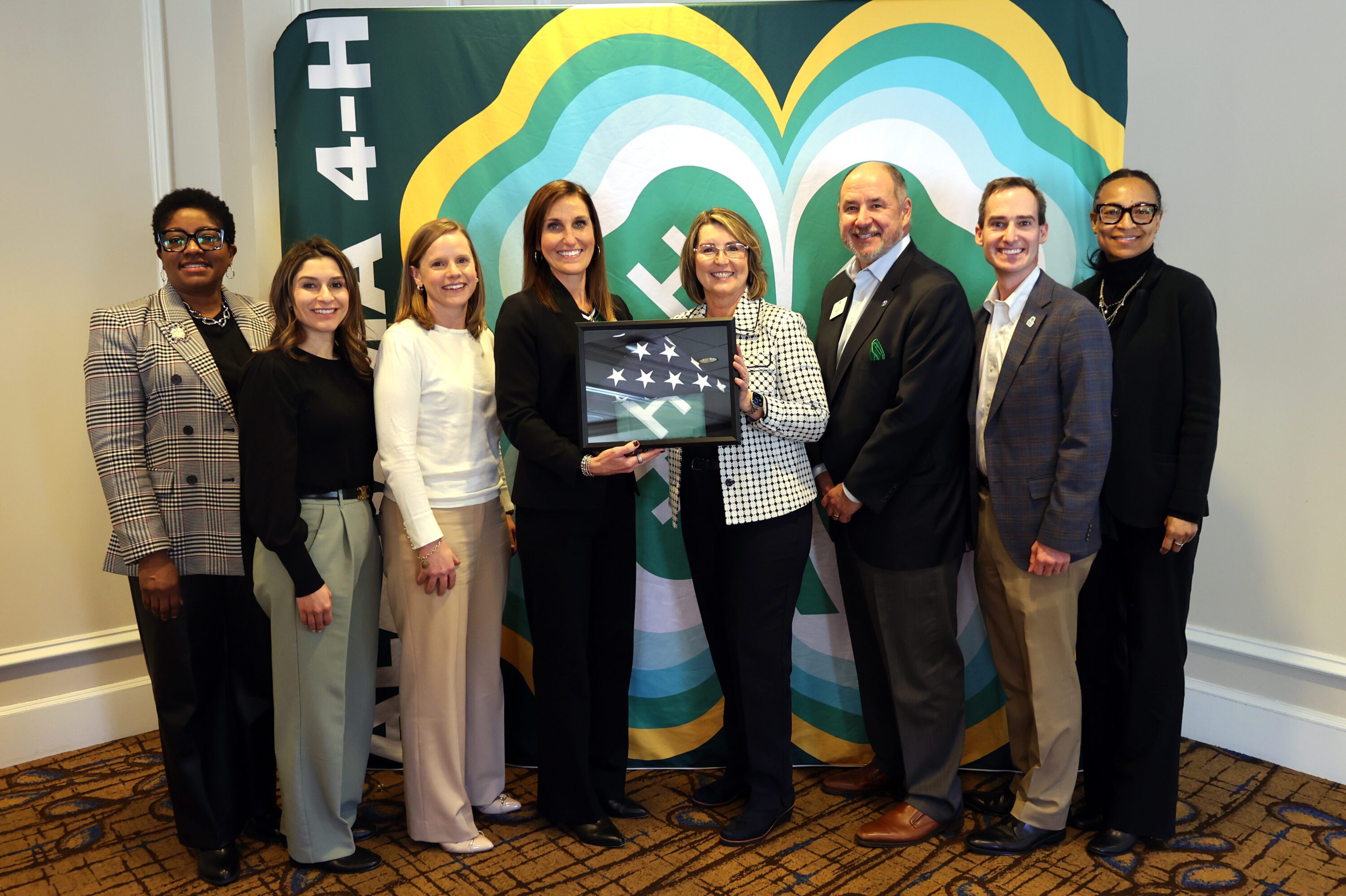 Auburn First Lady Tracy Roberts and Assistant Director for Alabama 4-H Casey Mull presented National 4-H Council President and CEO Jill Bramble with American and 4-H flags. From left are National 4-H Council Chief People Officer Shawnda Howard, Chief of Staff Eliza Hernandez, Chief Development and Marketing Officer Heather Elliott and Bramble; Roberts; National 4-H Council Chief Strategy Officer Andy Ferrin; Mull; and National 4-H Council Vice President of Communications Natalie Godwin.