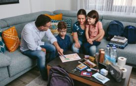 A family sitting on a couch around a coffee table that is stocked with emergency supplies. They are reviewing an emerency plan.