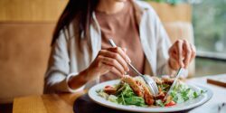 woman smiling eating chicken salad in a restaurant.