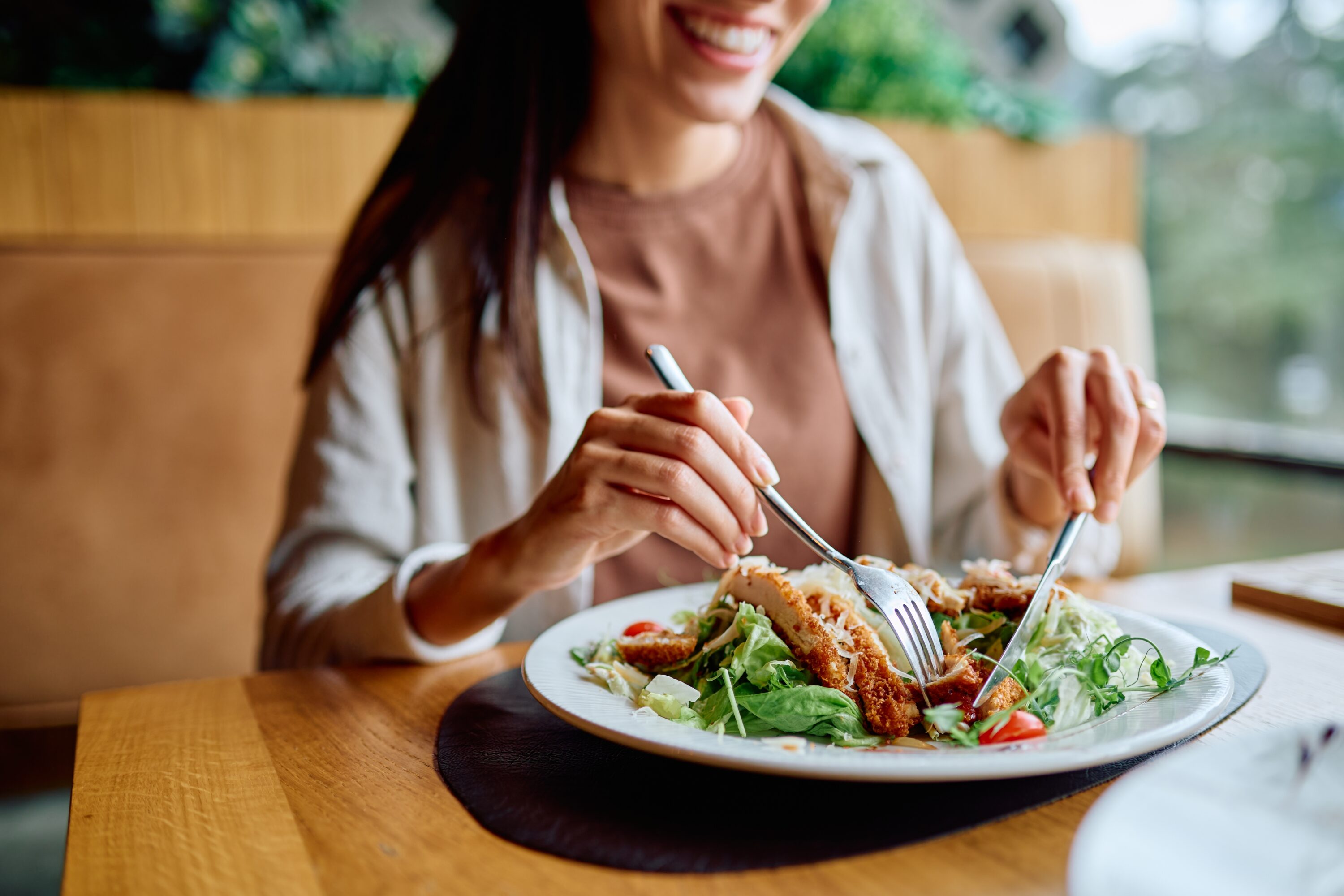 woman smiling eating chicken salad in a restaurant.