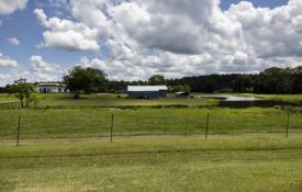 A rural scene with a fence-lined pasture in the foreground and a barn and home in the background.