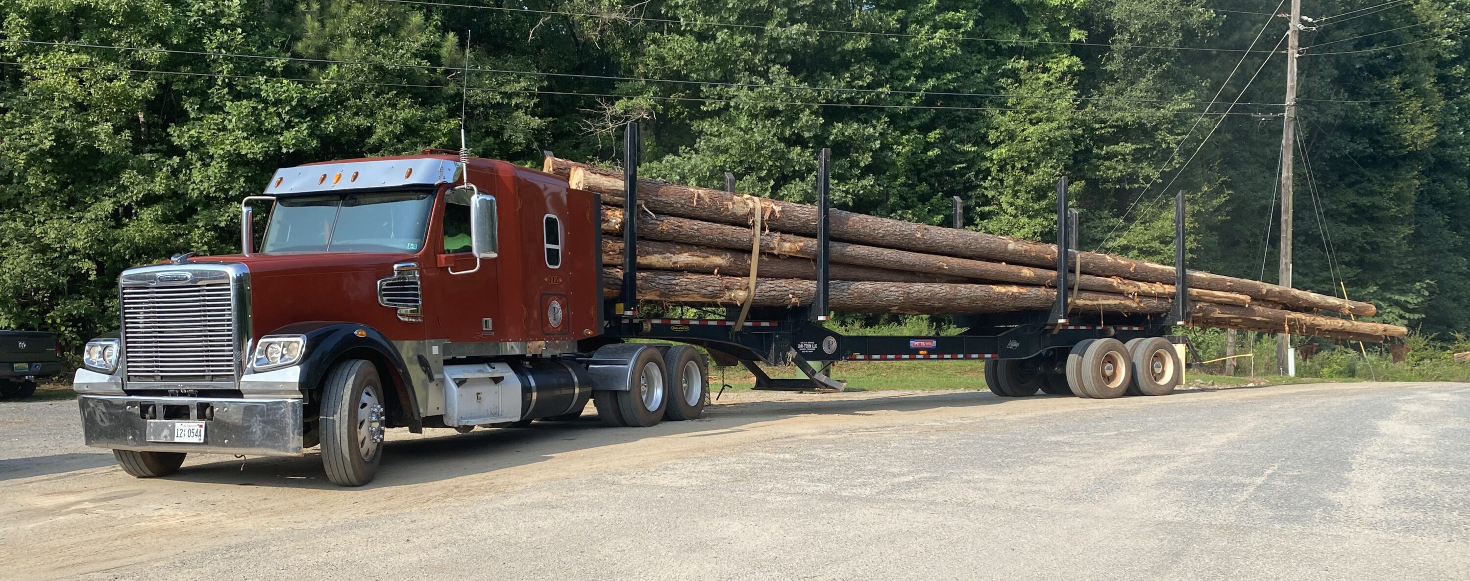 A red logging truck loaded down with logs.