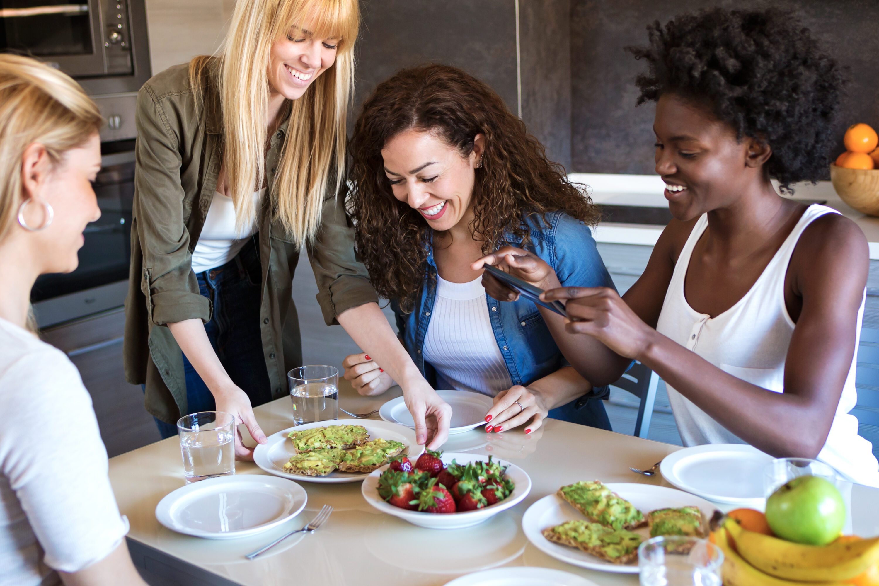 A group of four friends laughing while eating healthy food.