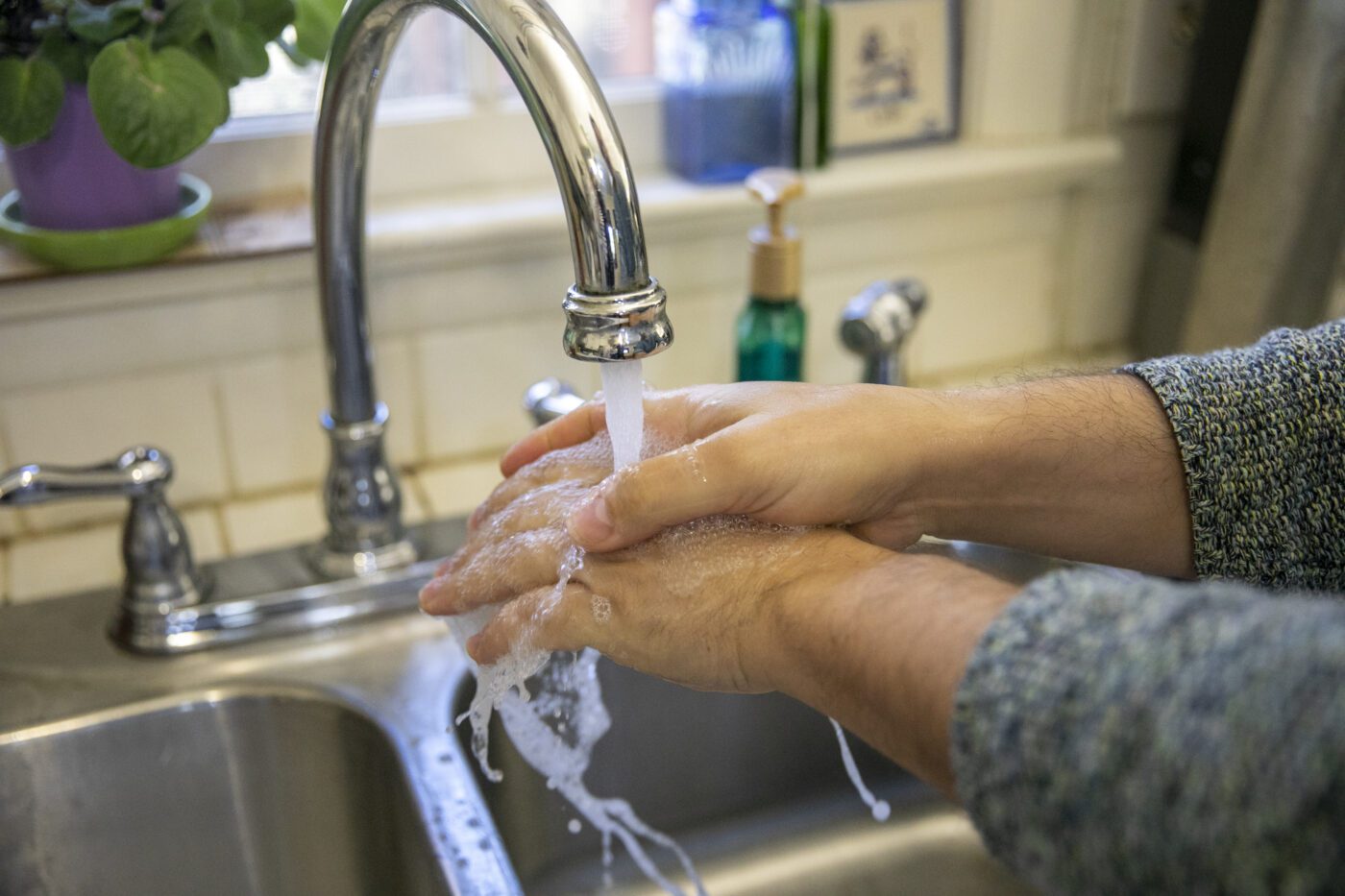 A closeup of someone washing their hands under a kitchen faucet.