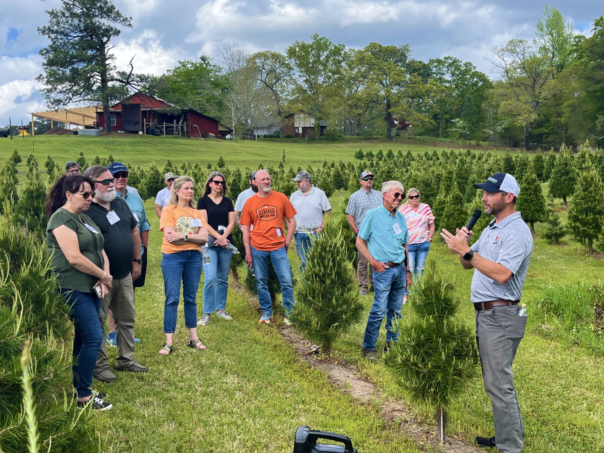 Figure 1. Jeremy Pickens speaks to a group of participants at a Christmas Tree Growers Workshop in central Alabama. Extension educator speaks to a group of adults standing in rows of young evergreen trees during an outdoor Christmas tree workshop on a farm.