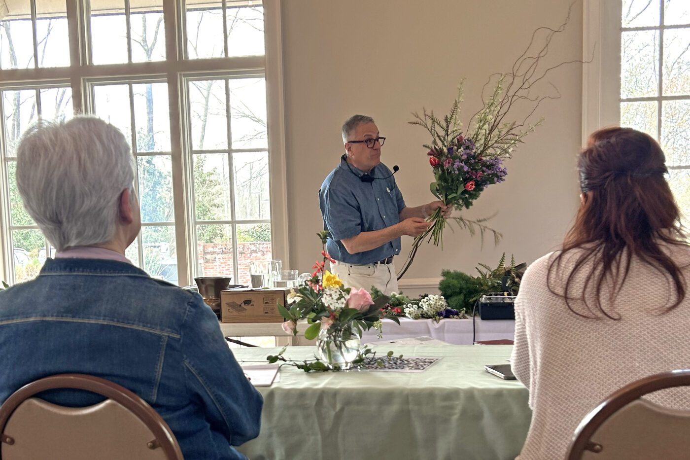 Jim DelPrince arranges a floral bouquet as two people in the foreground look on.