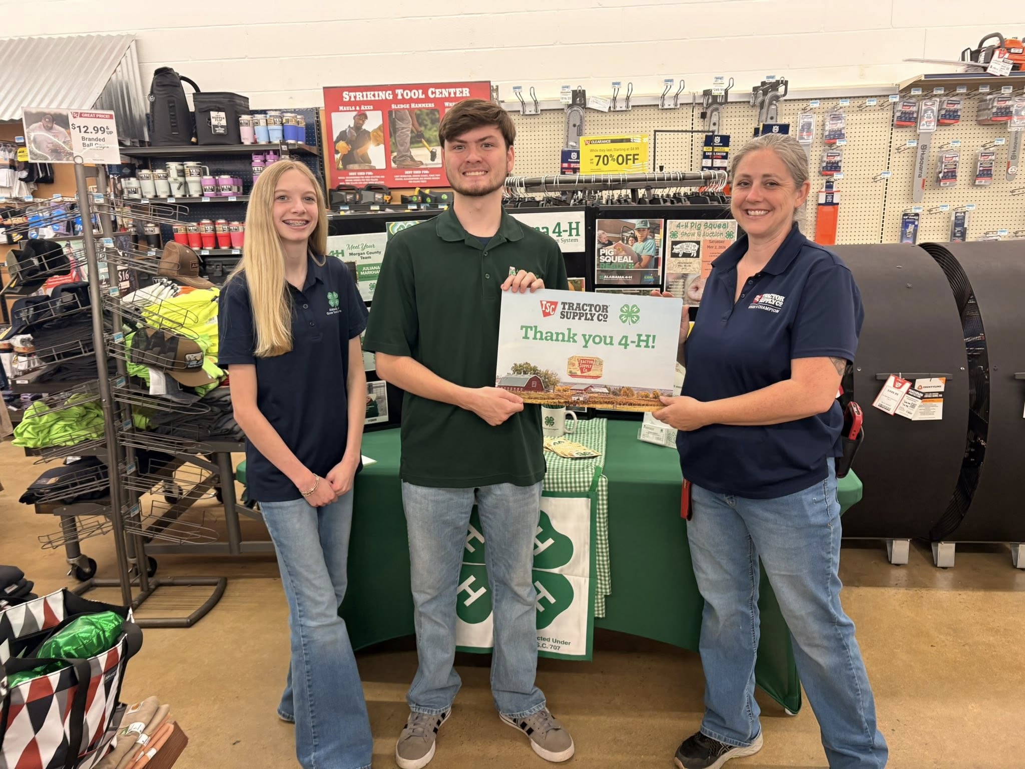 A group of three people inside a Tractor Supply store holding a sign that reads Thank you 4-H.