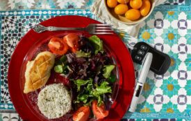 A red plate filled with vegetables, a lean protein, and rice. Also, a small bowl of citrus and a diabetes monitor.