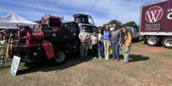 A group of students and volunteers stand beside a piece of heavy equipment from the Alabama Forestry Commission.