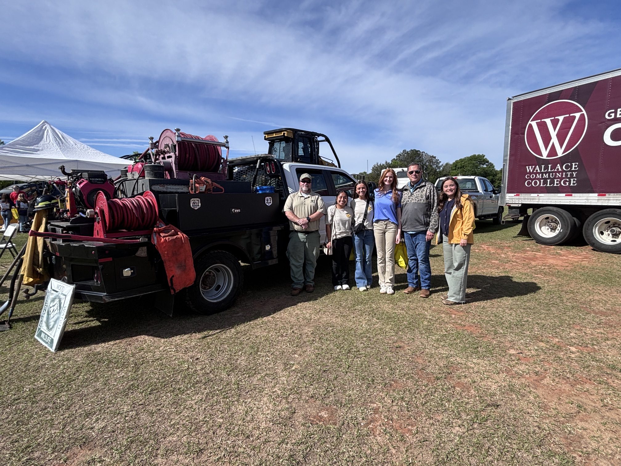 A group of students and volunteers stand beside a piece of heavy equipment from the Alabama Forestry Commission.