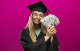 A young lady in a graduation cap and down holding cash.