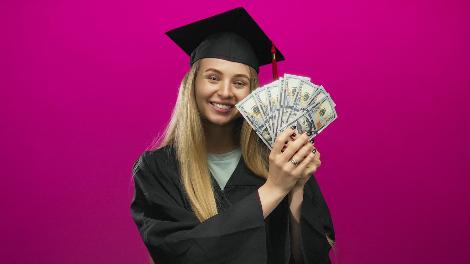 A young lady in a graduation cap and down holding cash.