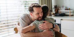 Dad hugging with daughter with diabetes in kitchen at home.