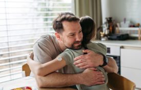 Dad hugging with daughter with diabetes in kitchen at home.