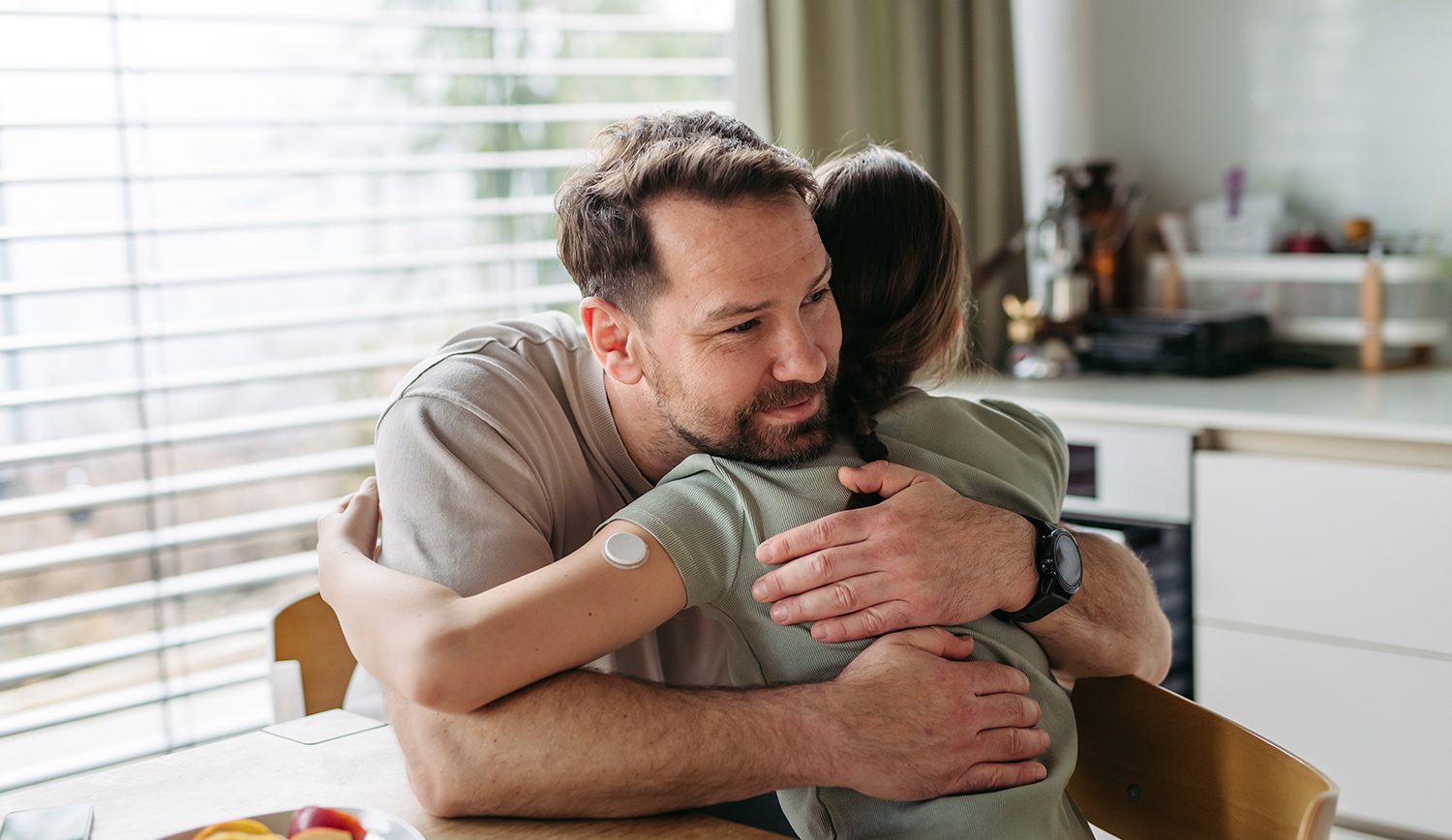 Dad hugging with daughter with diabetes in kitchen at home.