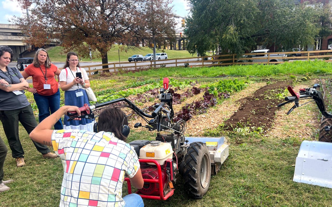 People watching a tilling demonstration in a garden.