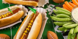 Game day table with hotdogs, a veggie tray, and miniature footballs.
