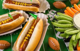 Game day table with hotdogs, a veggie tray, and miniature footballs.