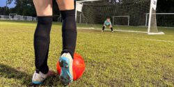 zoom in on soccer cleats about to kick a red soccer ball to the goal where a child goalie stands. image used to represent young athletes with type 1 diabetes
