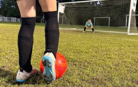 zoom in on soccer cleats about to kick a red soccer ball to the goal where a child goalie stands. image used to represent young athletes with type 1 diabetes