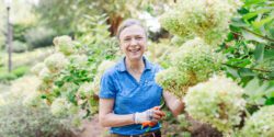 Kerry Smith holds pruning shears by a large hydrangea plant