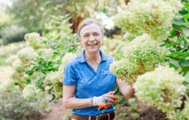 Kerry Smith holds pruning shears by a large hydrangea plant