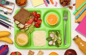 Serving tray of healthy food and stationery on white wooden table, flat lay. School lunch for farm to school