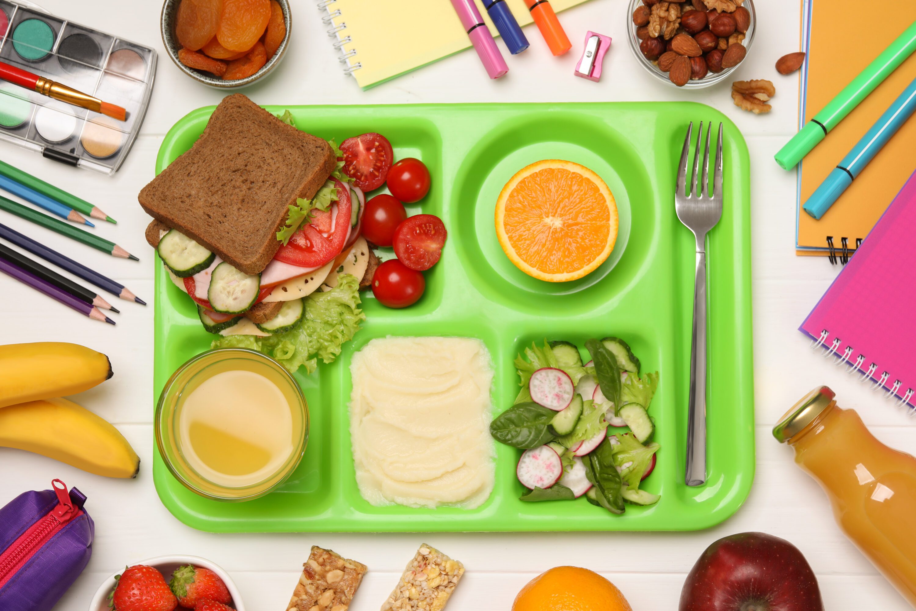 Serving tray of healthy food and stationery on white wooden table, flat lay. School lunch for farm to school
