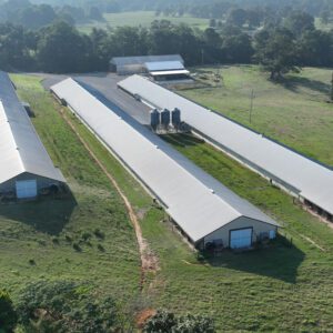 An aerial view of a four-house commercial broiler farm on terrain that slopes from highest to lowest points. The storage bladder is on the lowest terrain.