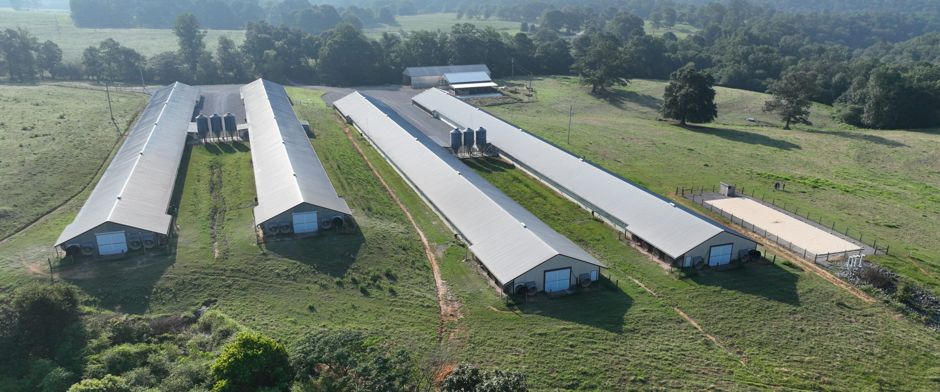 An aerial view of a four-house commercial broiler farm on terrain that slopes from highest to lowest points. The storage bladder is on the lowest terrain.