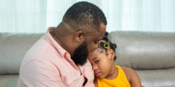 A fathering sitting on a couch and comforting his sad daughter.
